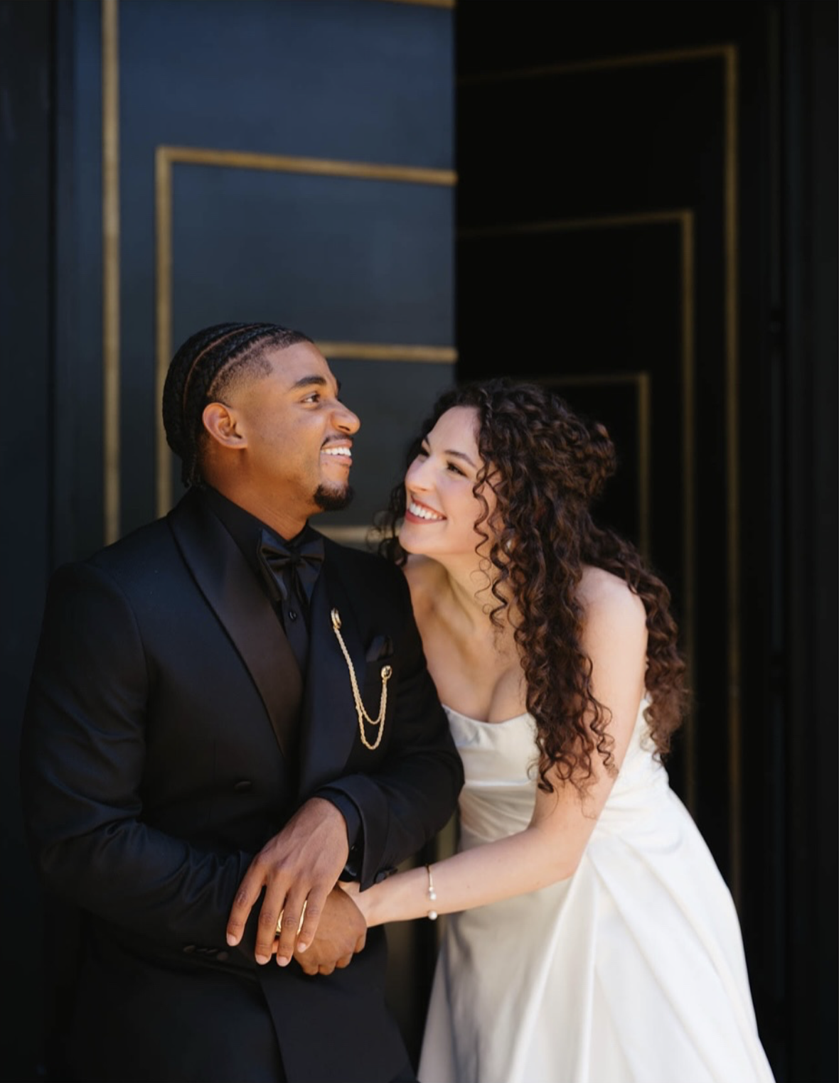 A happy couple, dressed in wedding attire, sharing an intimate moment and smiling at each other.