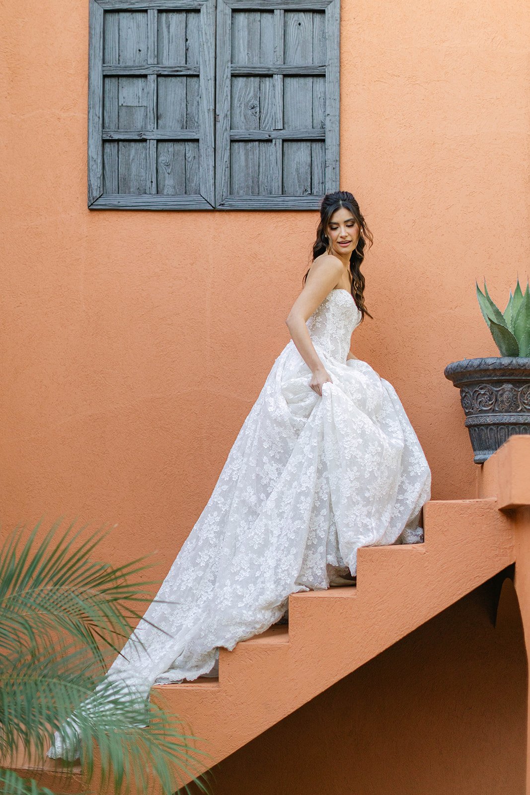A bride in a long white dress climbing an orange staircase at Agave Estates in Houston TX
