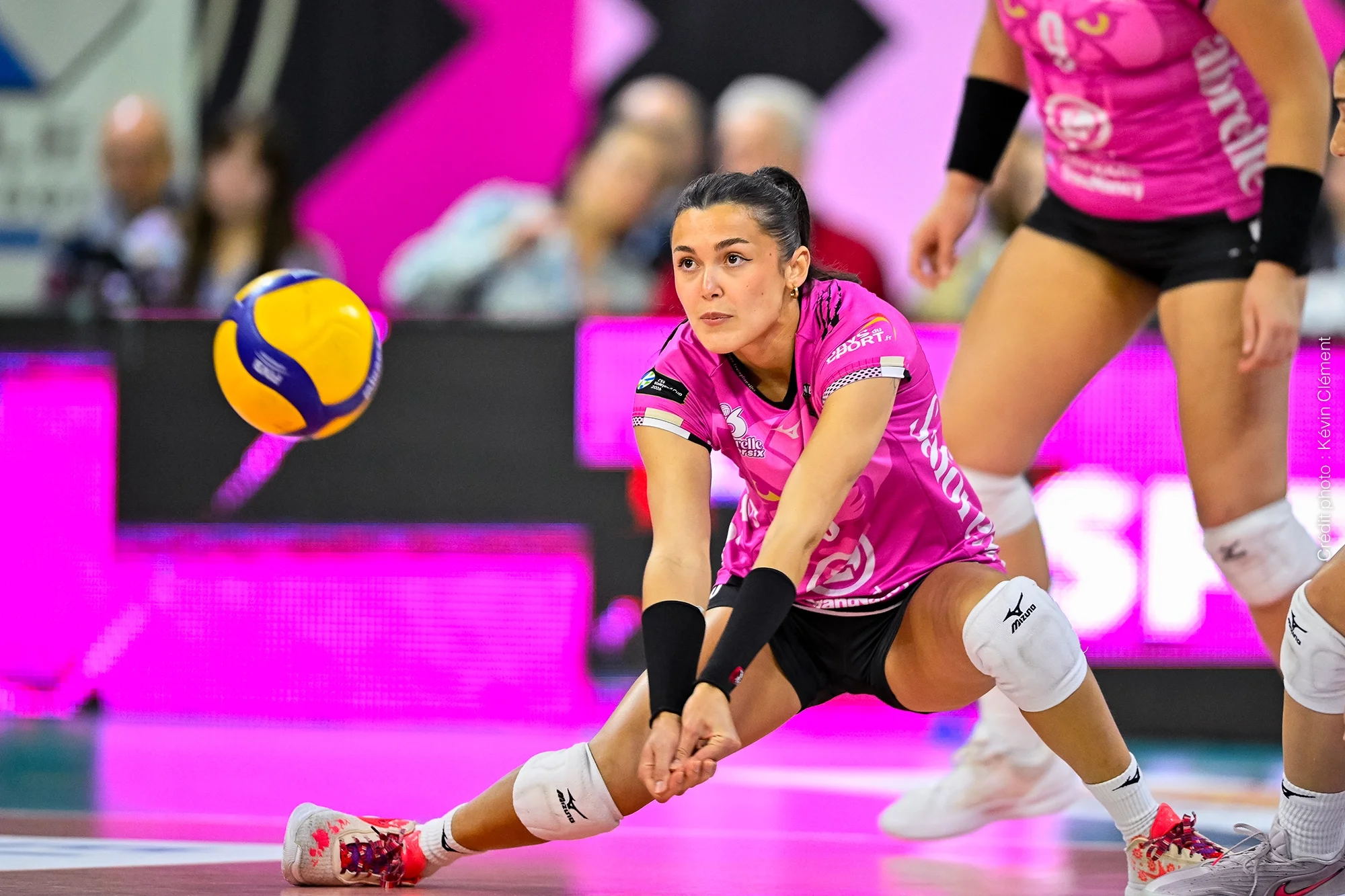 Joueuse du club de volley féminin VNVB en action de défense et réception lors d’un match au Palais des Sports de Nancy, sous l’identité visuelle rose et noire conçue par Studio 422