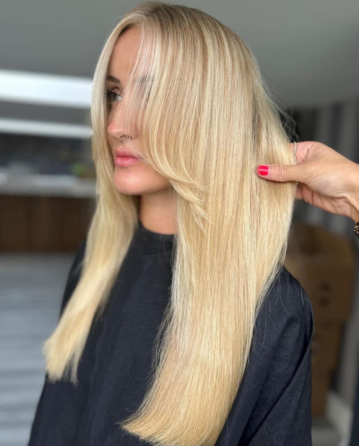 Hairdresser styling a woman’s long, straight blonde hair in a salon.