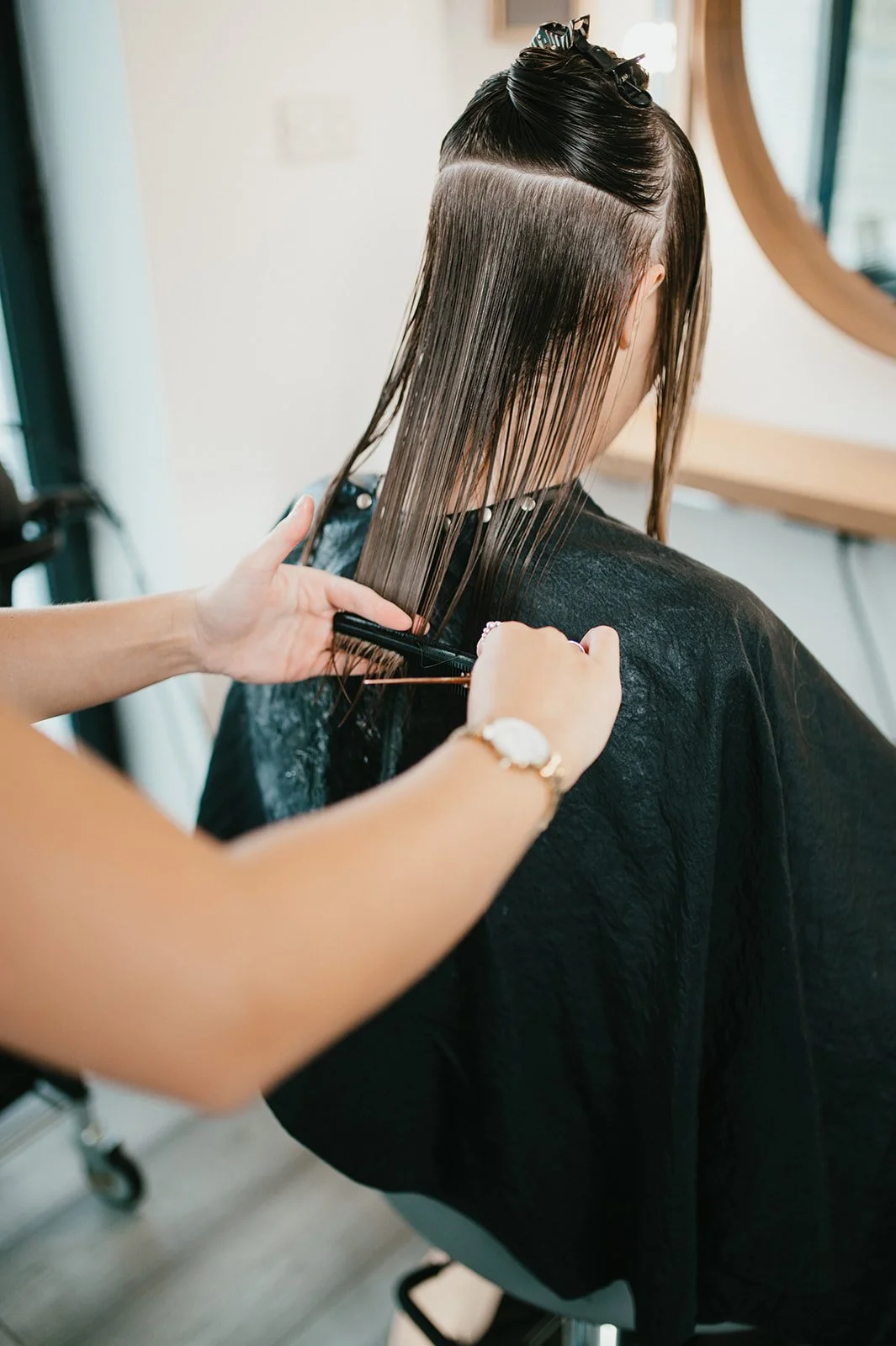 A person getting their hair cut at a salon, with long straight hair being sectioned and cut by a hairstylist.