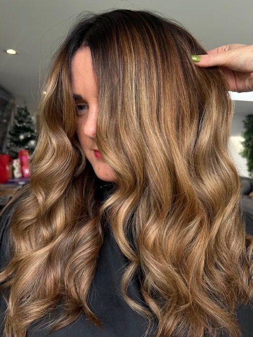 Woman with long, wavy, light brown hair with blonde highlights, touching her hair with one hand.