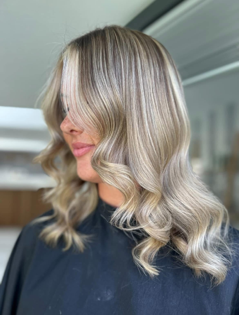 Woman with shoulder-length, wavy blonde hair in a salon.