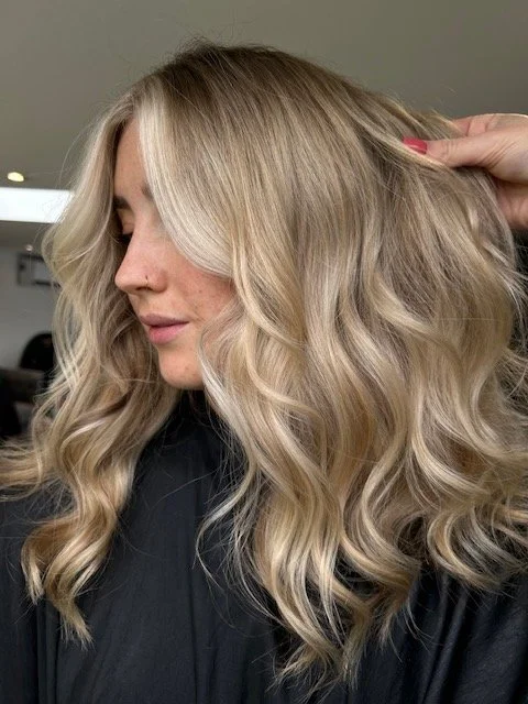 Woman with long, wavy blonde hair in a salon, being styled.