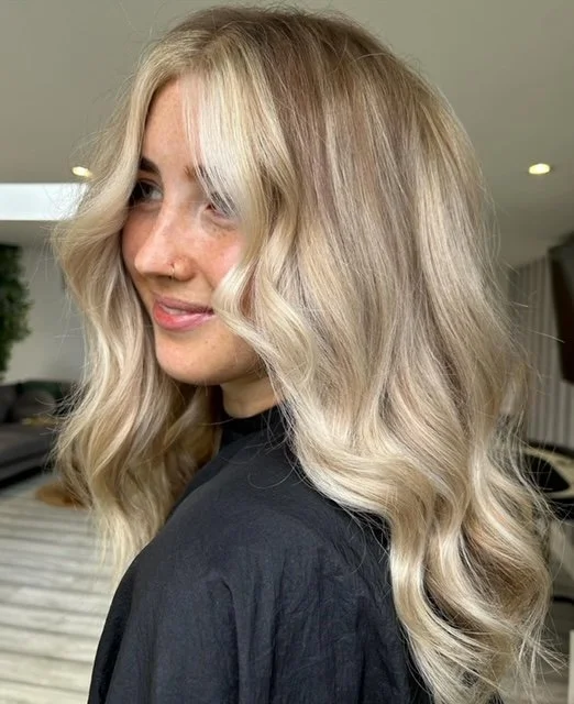 Woman with wavy blonde hair and a black top in an indoor setting.