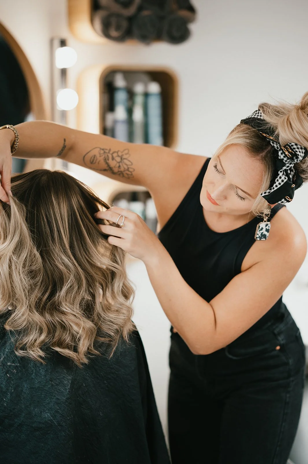 Hair stylist working on a woman's blonde, wavy hair in a salon.