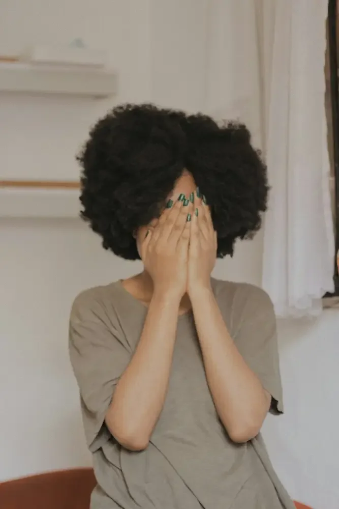 A woman with an afro covers her face with her hands.