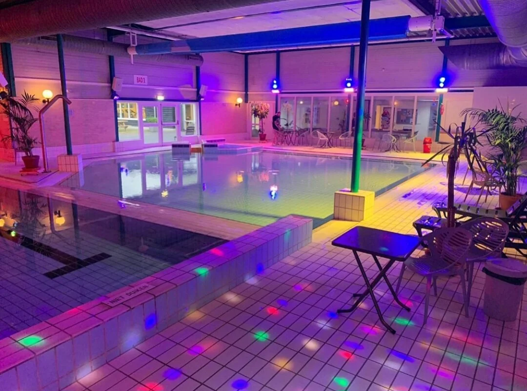 Interieur van een zwembad met kleurrijke LED-verlichting en ligstoelen.