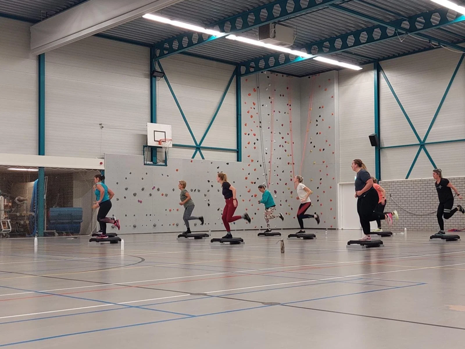 Mensen die in een sportschool oefenen op stepapparaten, met een klimwand op de achtergrond.