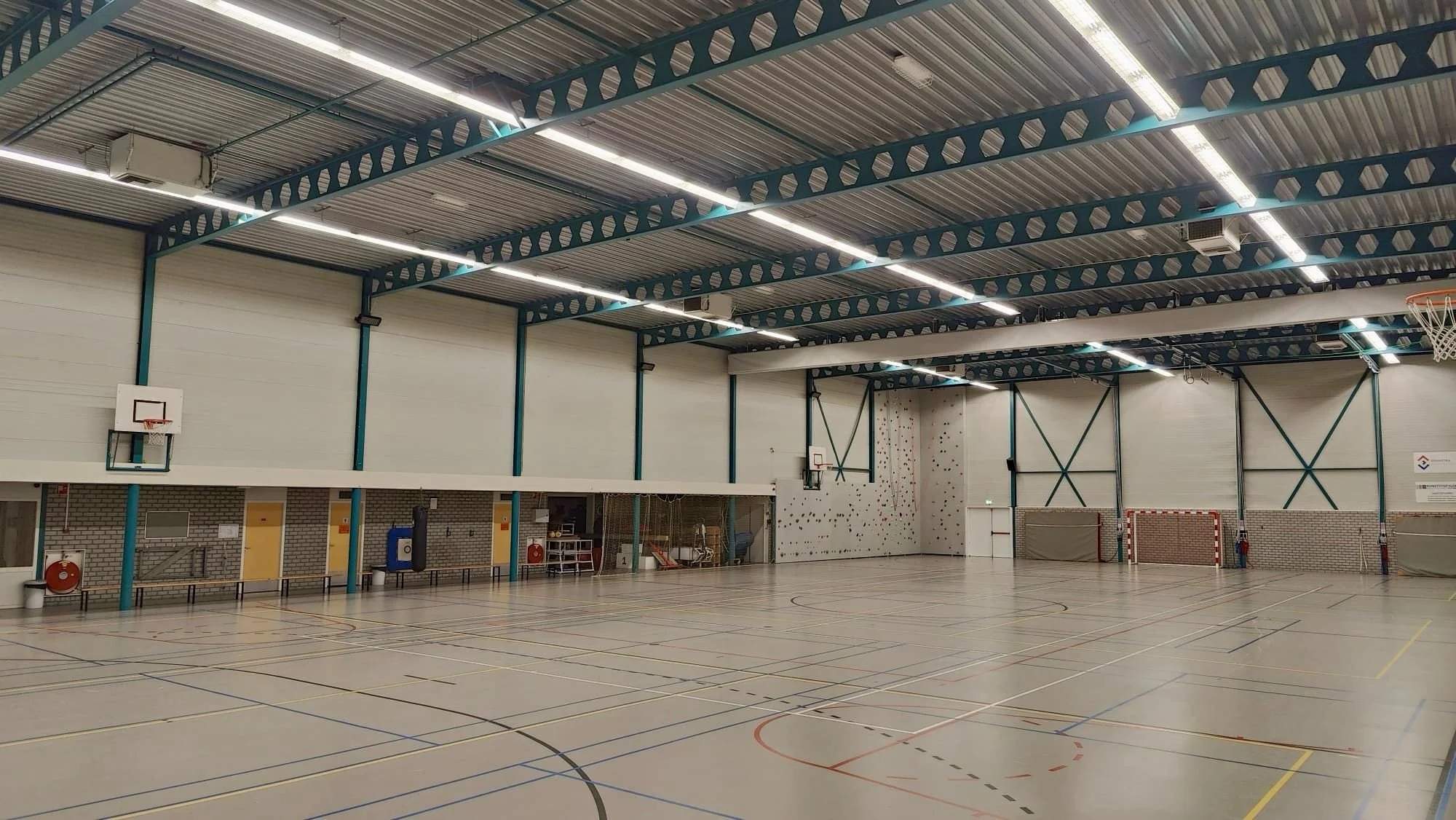 Leeg sporthal met basketbal- en volleybalvelden, klimwand en doelen voor zaalhockey.