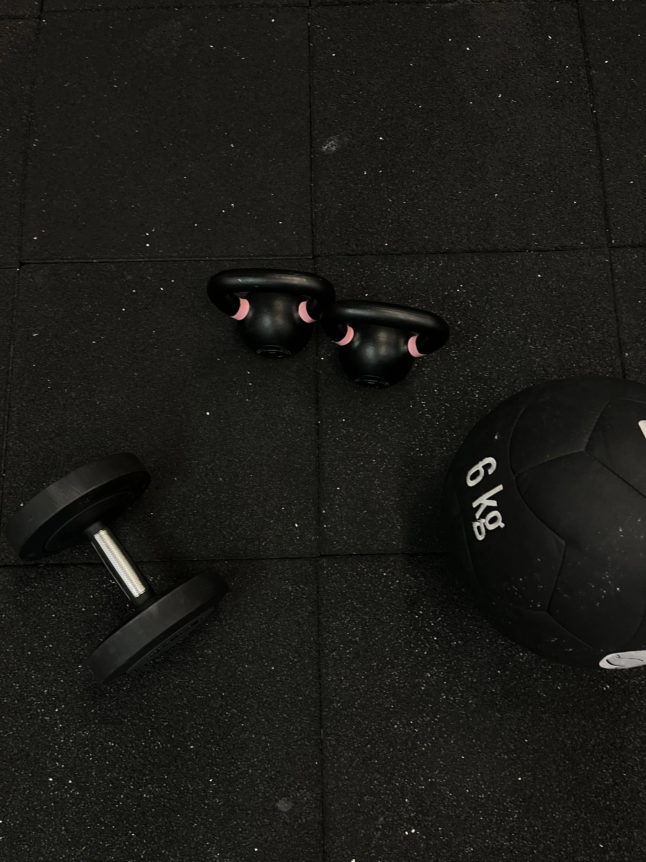 Kettlebell, dumbbell en medicinbal op een gymvloer.