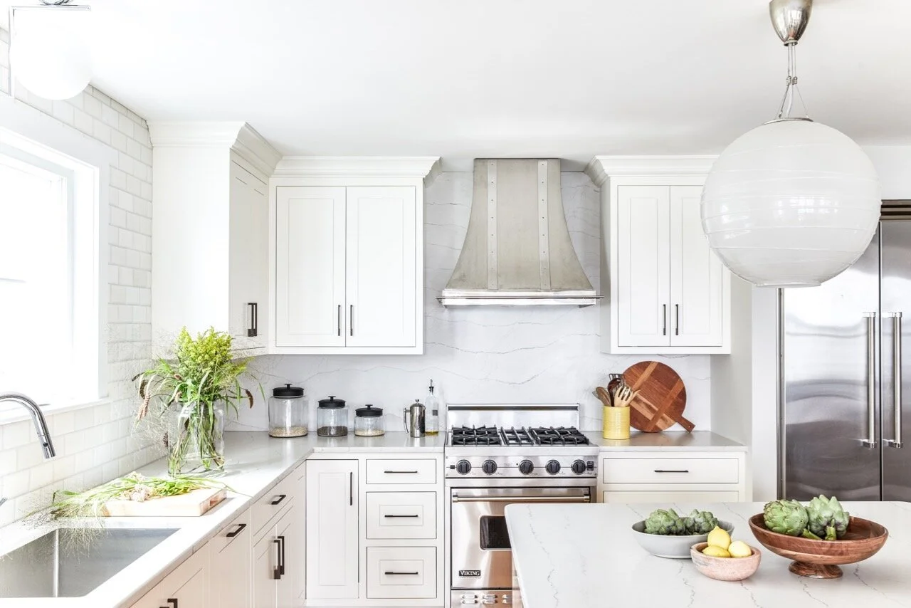 Modern kitchen with white cabinets, marble countertops, stainless steel appliances, and decorative artichokes on the island.