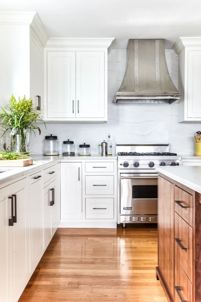 Modern white kitchen with stainless steel stove, white cabinets, wooden island, and hardwood floors.