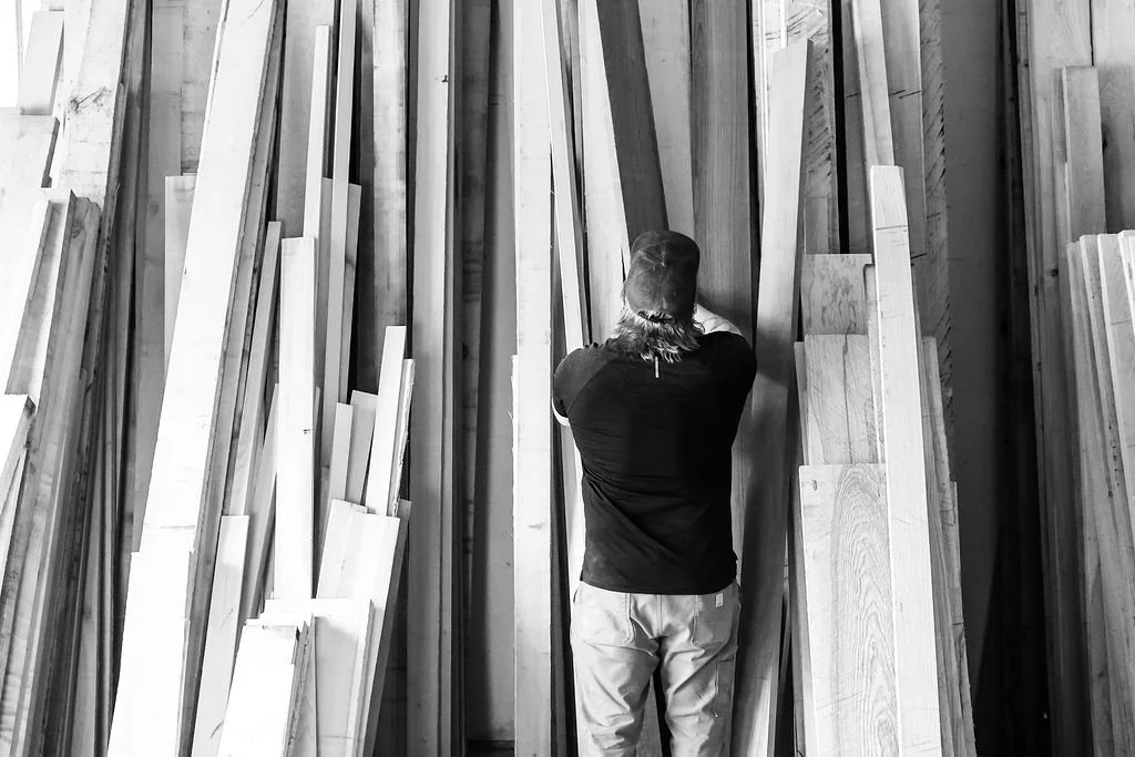 A man organizing or stacking wooden planks in a storage area or lumber yard.
