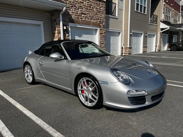 Silver Porsche convertible parked in a residential parking lot.