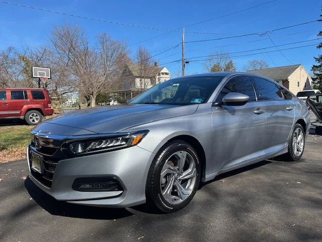 Silver sedan parked on a driveway with nearby houses and trees in the background.