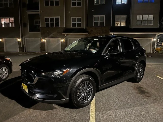 A black SUV parked in a parking lot at night with residential buildings in the background.