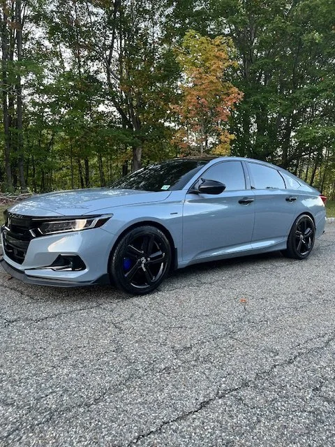 Light blue sedan parked on a cracked asphalt road with trees and autumn leaves in the background.