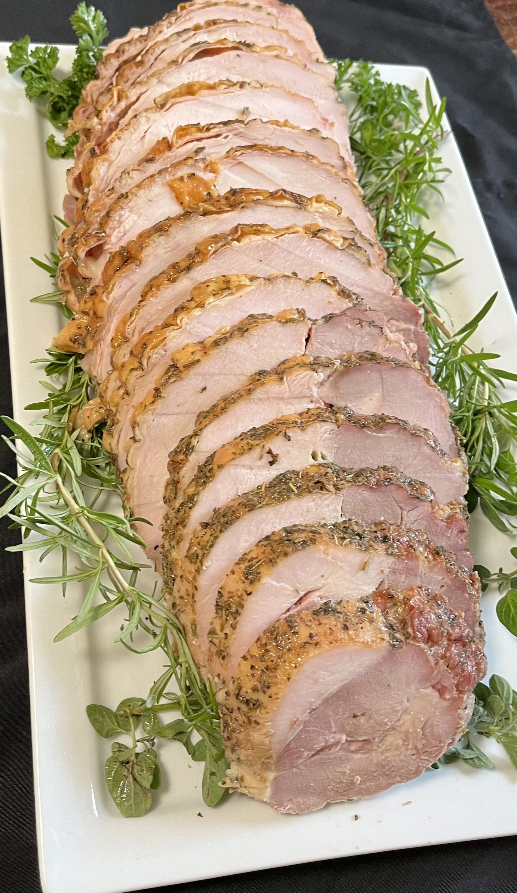 Sliced roasted pork tenderloin garnished with fresh herbs on a white platter.