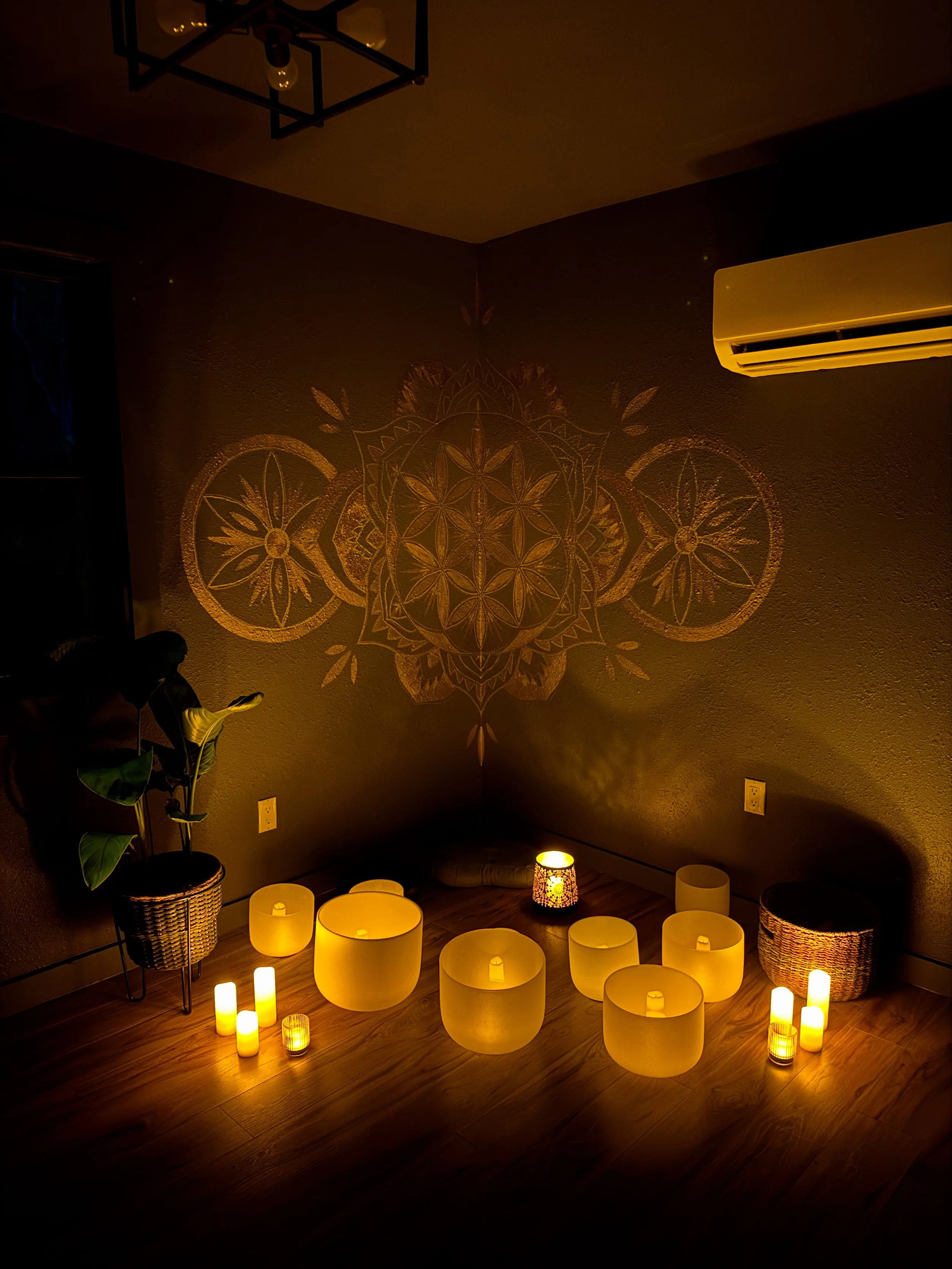 Crystal singing bowls surrounded by glowing candles beneath a gold Seed of Life geometric mural in the Dōm studio in Franklin, NC