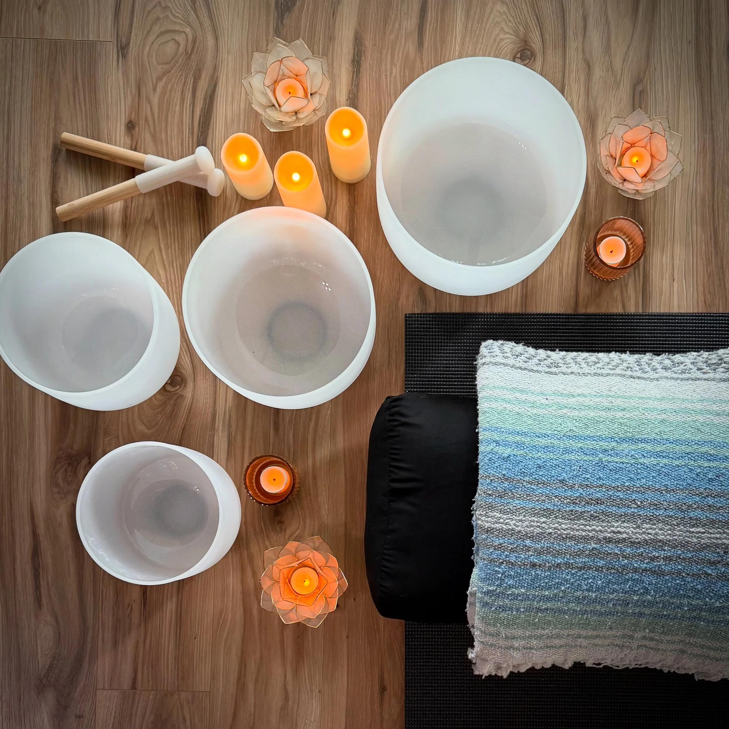A wooden table with decorative candles in flower-shaped holders, empty white bowls, and a black and multicolored striped cloth.
