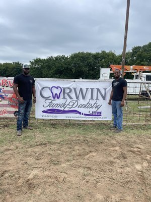Two men standing on grass holding a large banner for CW Family Dentistry and Orthodontics, with trees and a cloudy sky in the background.