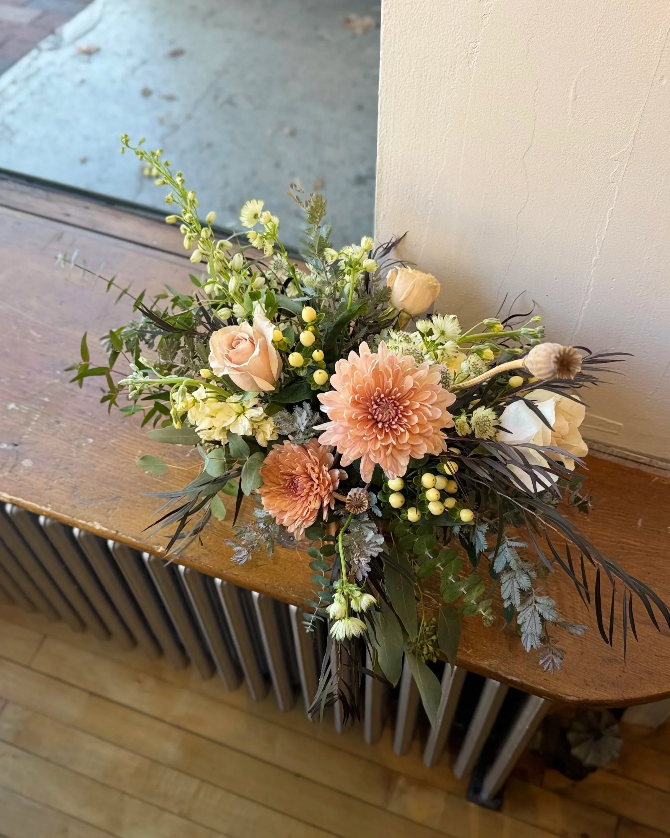 A floral arrangement with peach, cream, and white flowers on a wooden surface near a window.