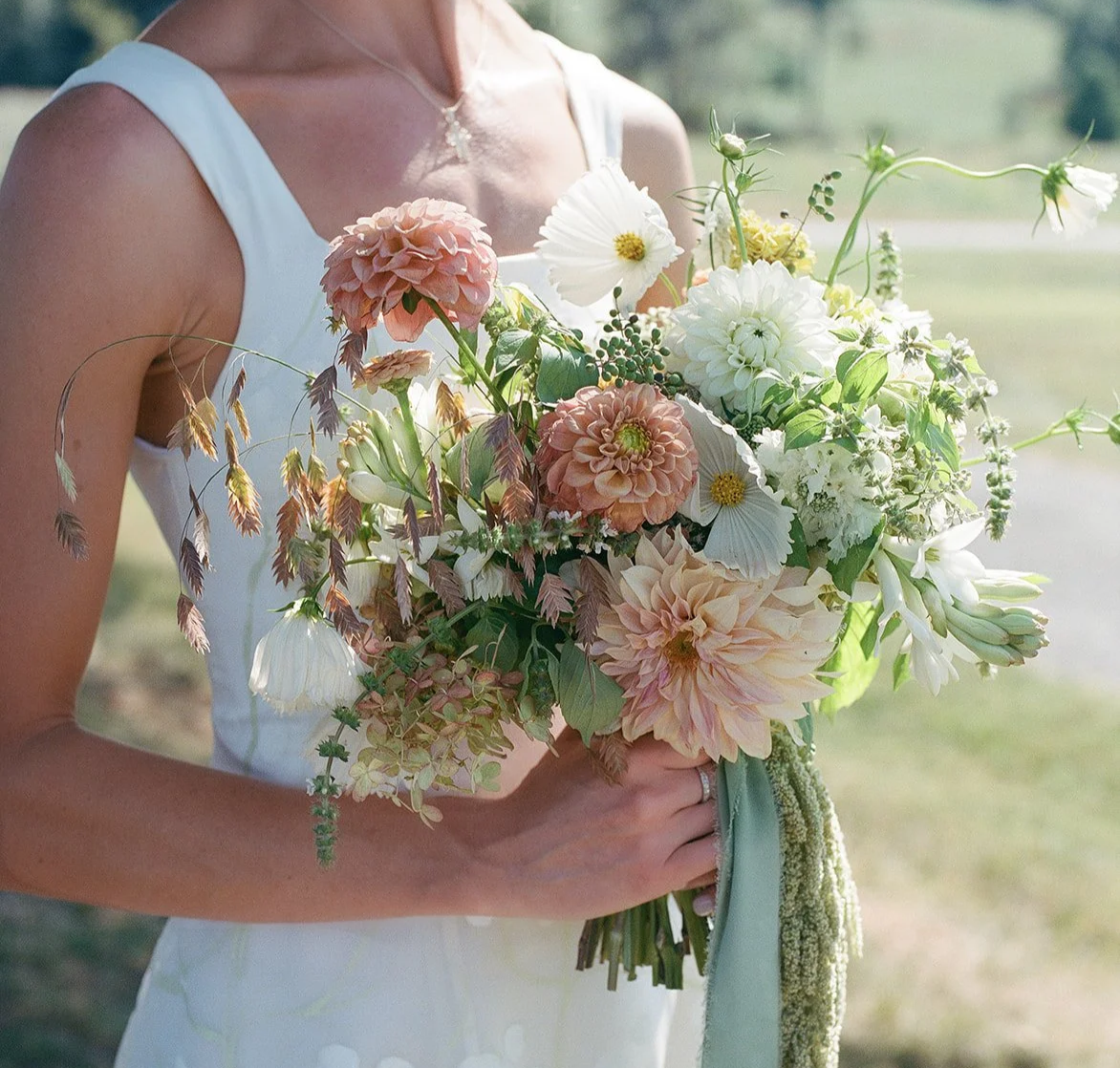 A woman in a white dress holding a large bouquet of pink and white flowers outdoors.