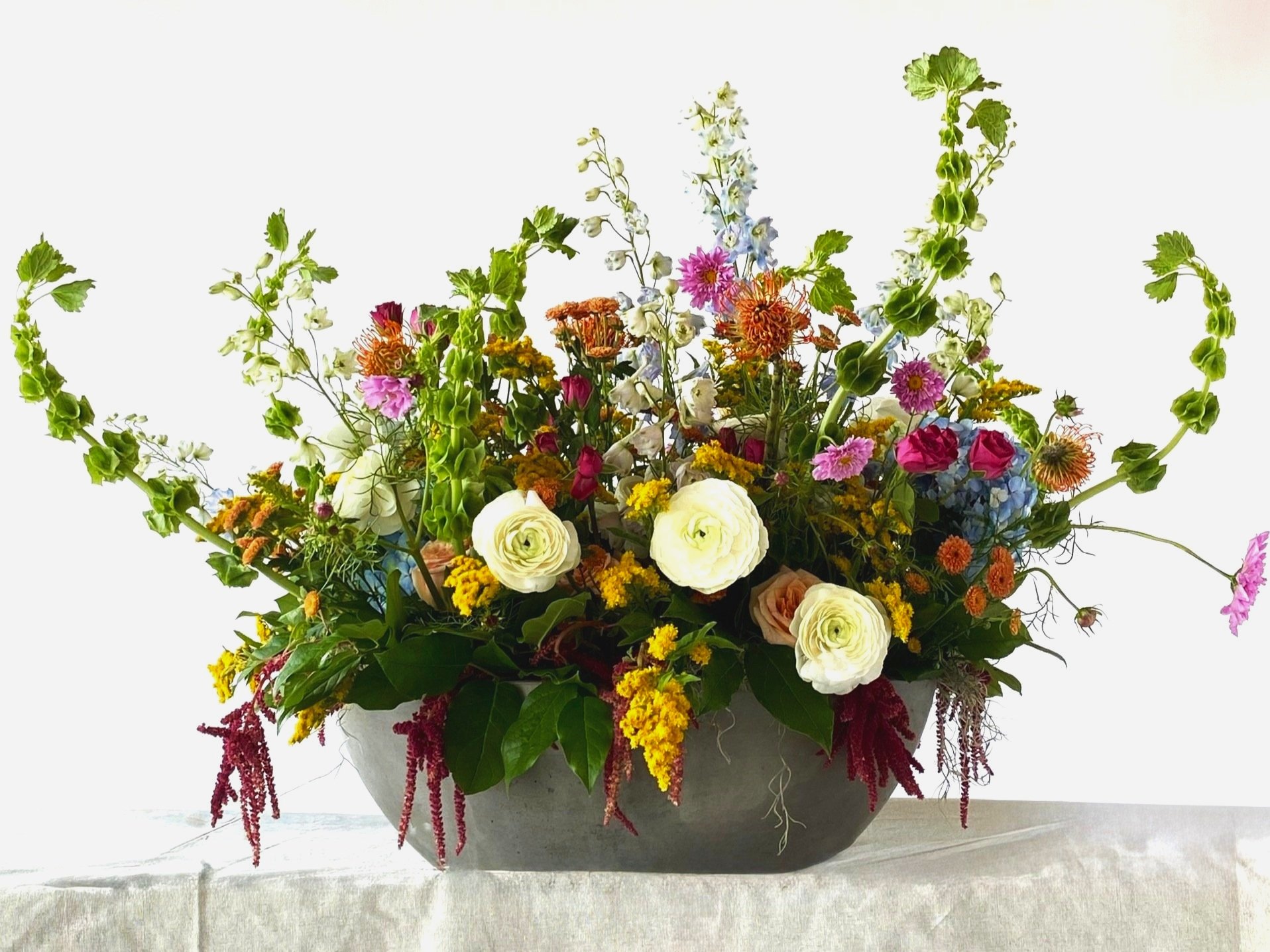 Colorful mixed flower arrangement in a gray oval vase, resting on a table with a light-colored tablecloth.