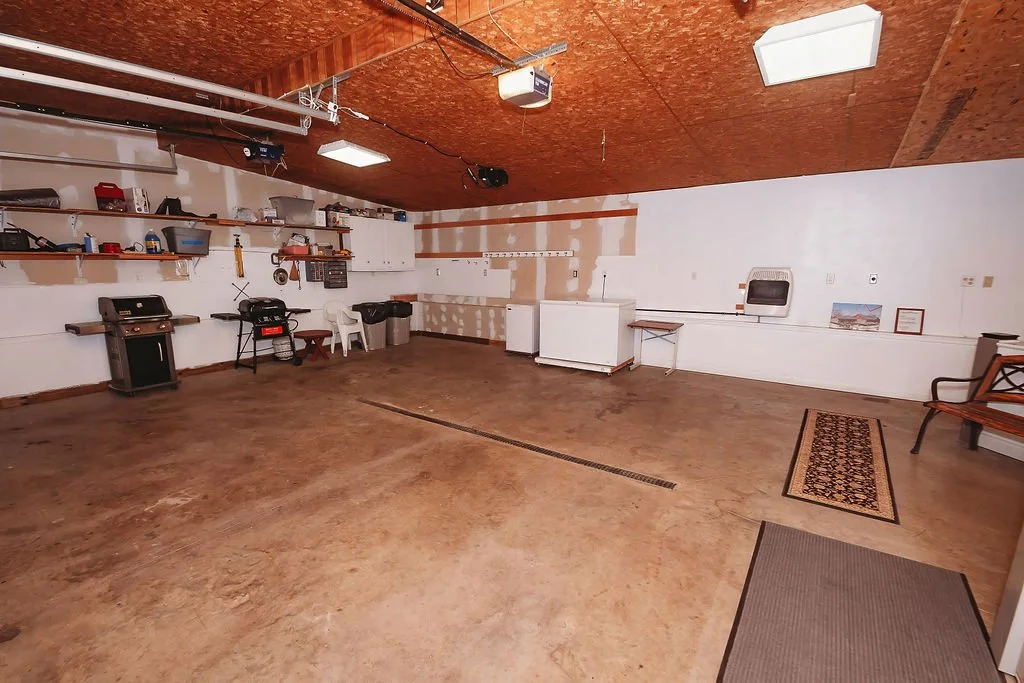 Empty garage with tools, shelves, a grill, and a bench against the white walls and brown ceiling.