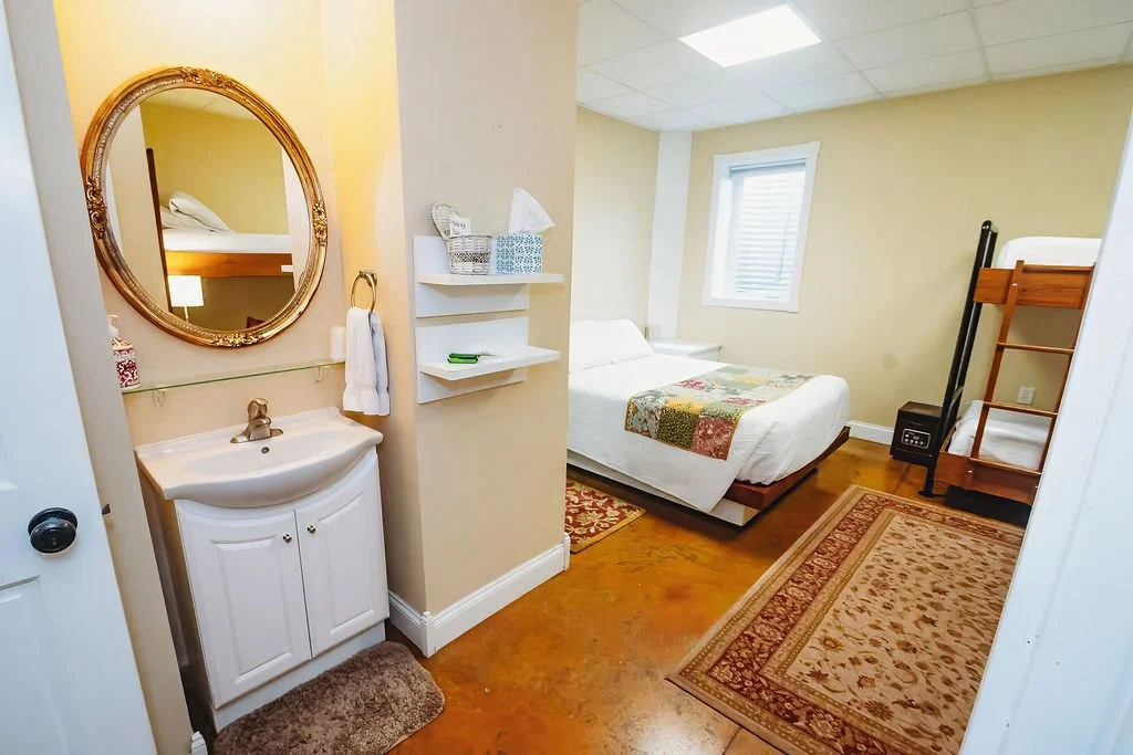 Small bedroom with a bed, a bunk bed, a window, and a small white sink with a mirror on the wall.