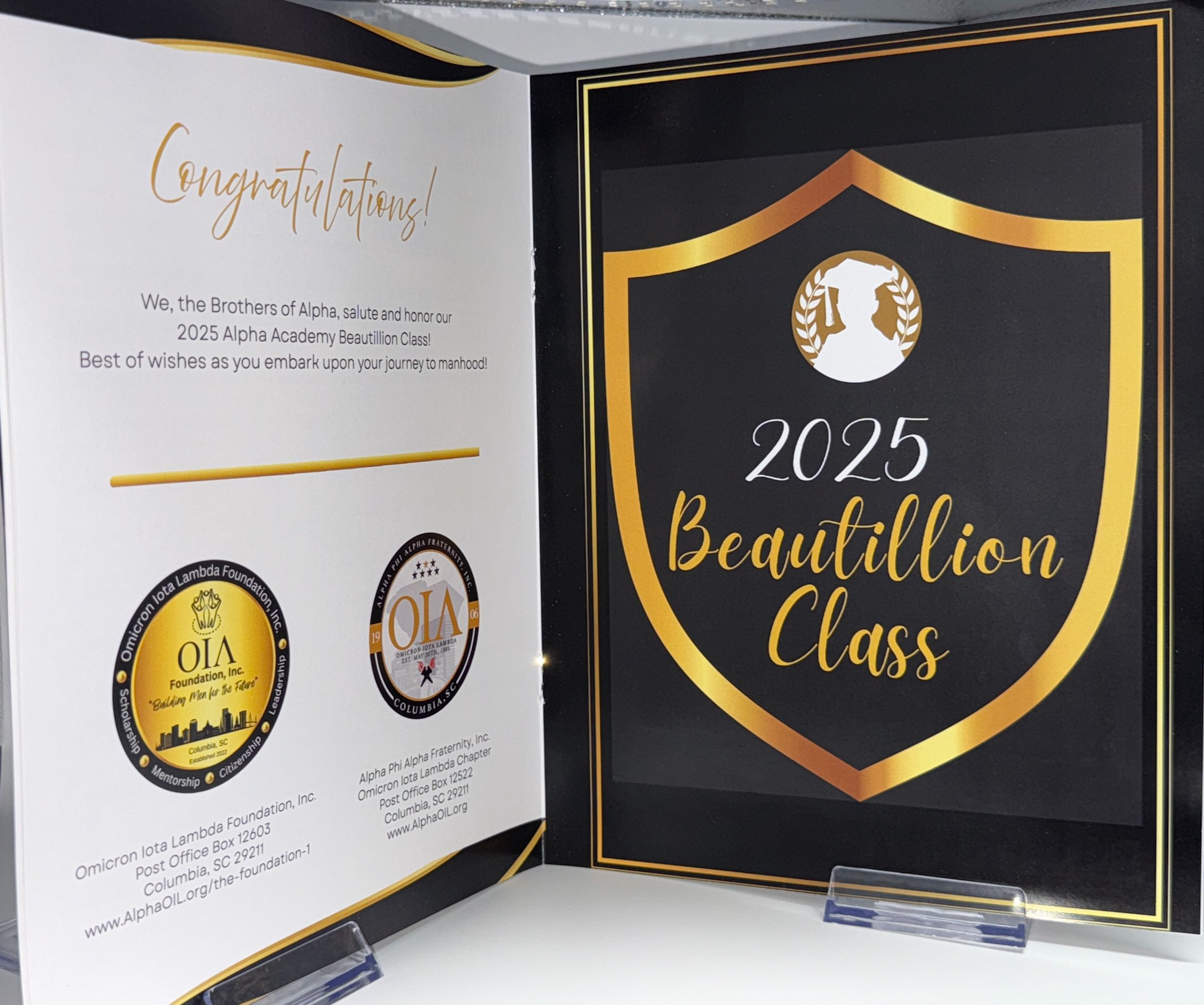 Open booklet displaying a congratulatory message for the 2025 Alpha Academy Beautillion Class, with logos of the Omicron Iota Lambda Foundation and Omicron Iota Lambda Chapter, featuring gold and black design elements.