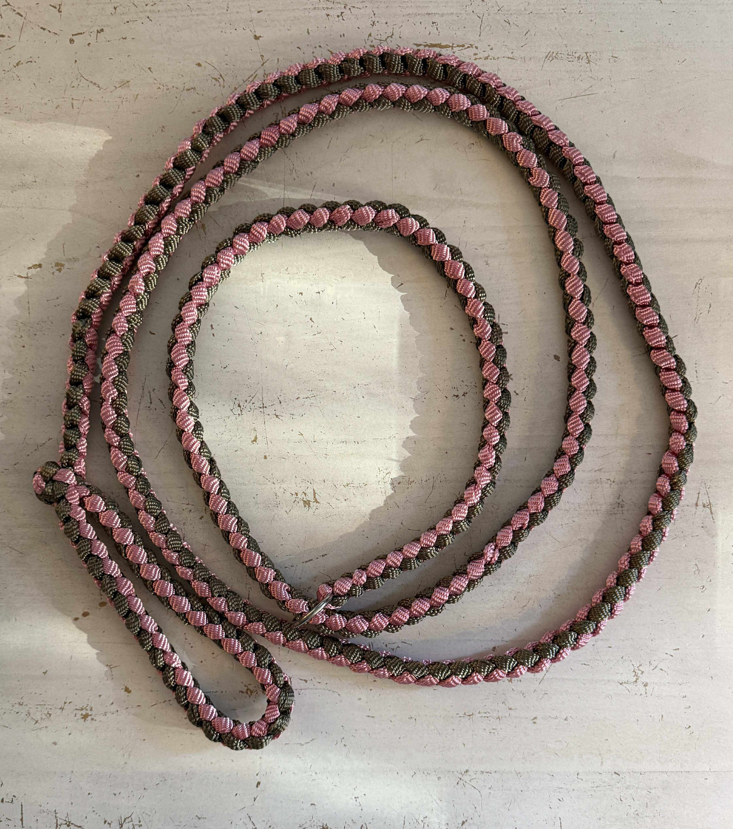 A pink and black braided paracord leash on a white wooden surface.