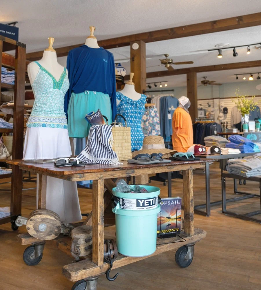 Display of athletic clothing, hats, and accessories in a retail store with wooden fixtures and flooring.