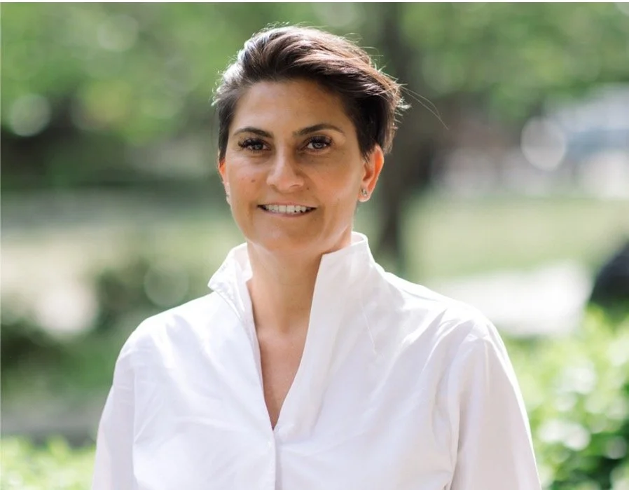 A headshot of Rebecca Paisis, the CEO, in a white shirt against a blurred park background