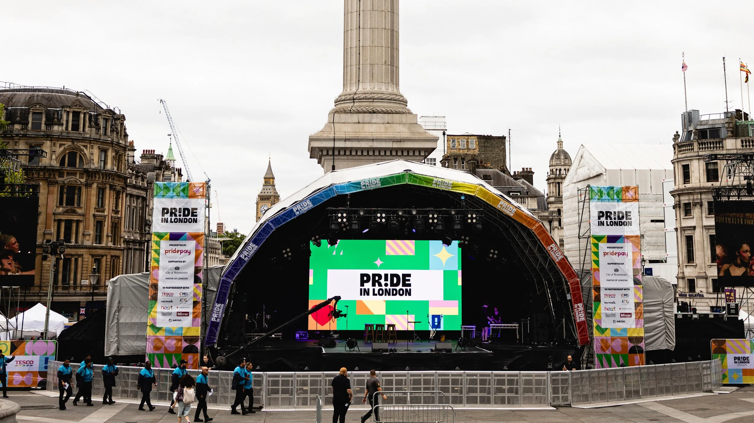 The Pride in London main stage in Trafalgar Square, positioned directly in front of Nelson's Column. The stage features a large digital screen displaying the "PRIDE IN LONDON" logo with vibrant geometric patterns..