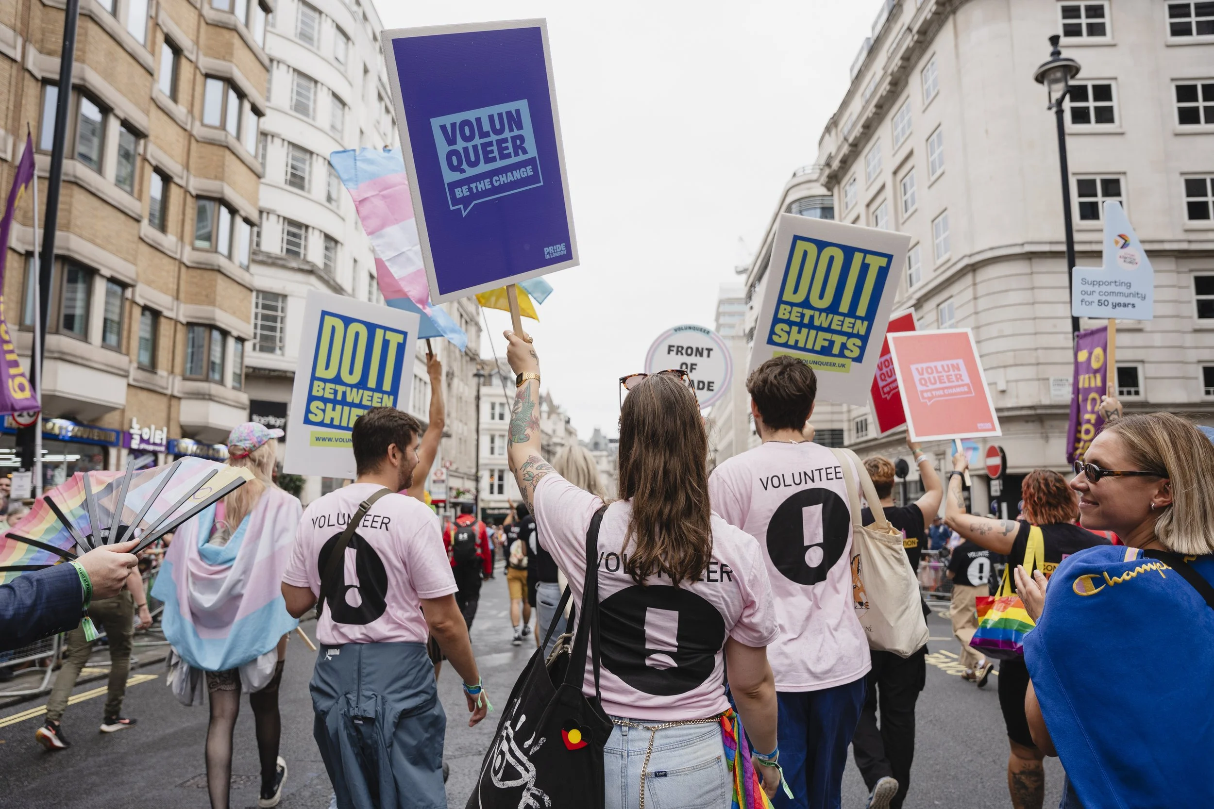 Three Pride in London volunteer stewards holding the 2025 "Volunqueer" placards