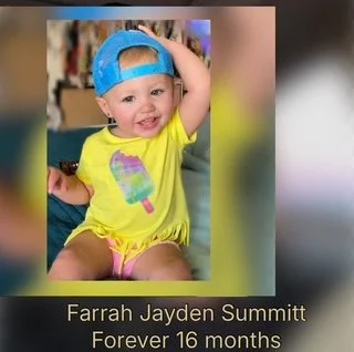 Smiling young girl wearing a blue baseball cap backward and a yellow outfit with a colorful popsicle graphic, sitting indoors.