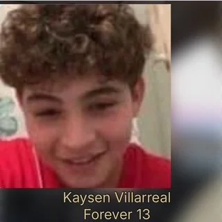 A smiling boy with curly hair wearing a red shirt.