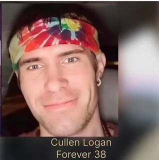A young man wearing a colorful tie-dye headband, with dark hair, light skin, earrings, and a slight smile, sitting in a car.