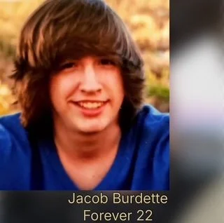 A young man with medium-length brown hair, smiling, wearing a blue shirt, outdoors with blurred background. Caption reads "Jacob Burdette Forever 22."