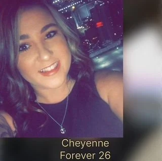 A young woman with curly hair smiling at the camera, wearing a black top and a necklace, with city lights in the background. Caption reads 'Cheyenne Forever 26'.