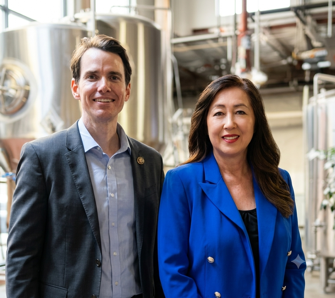 Two professionals, a man and a woman, standing in an industrial brewery with stainless steel tanks in the background.