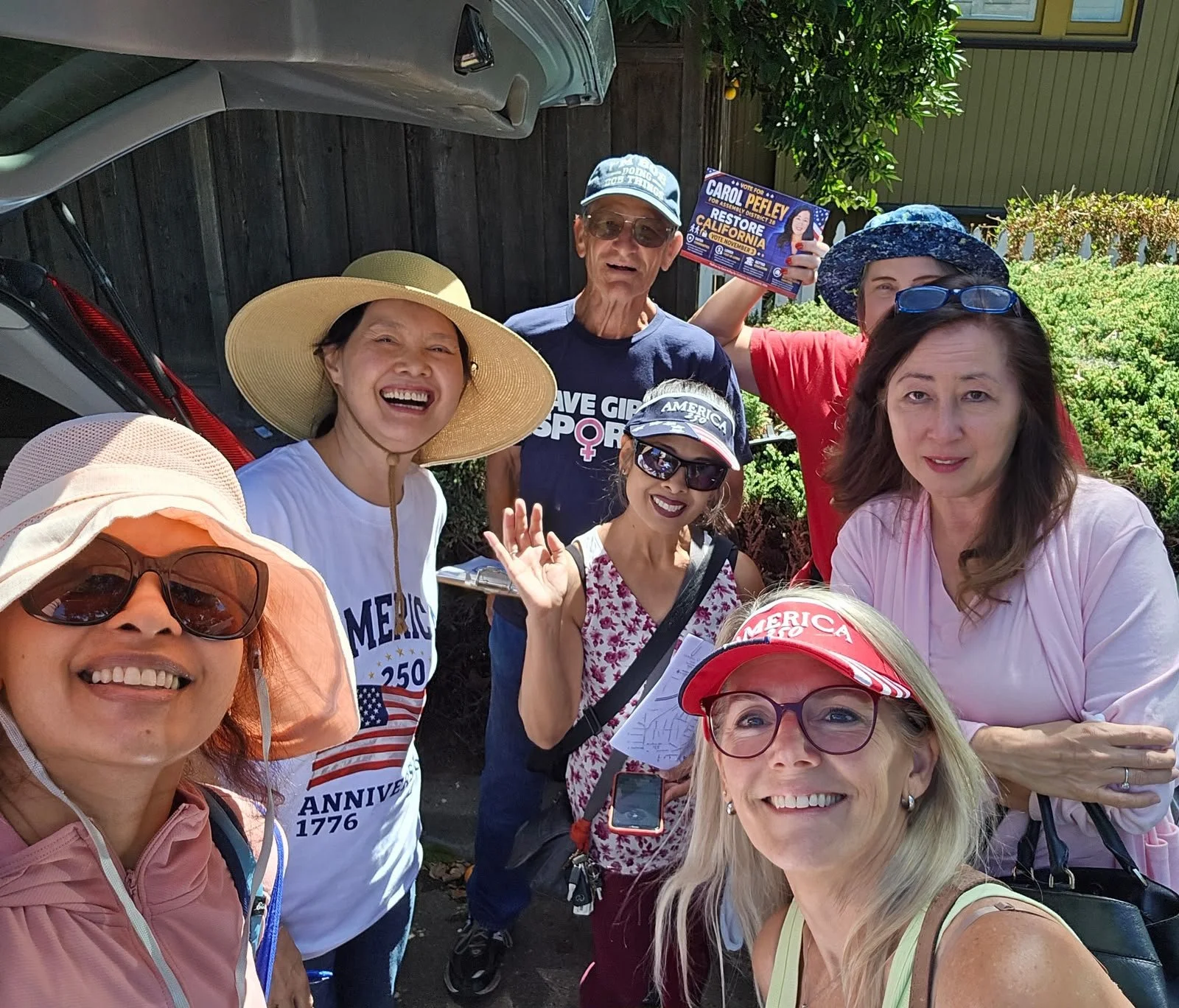Group of smiling women and one man taking a selfie outdoors, with some wearing hats, sunglasses, and campaign items supporting Carol Pefley for California Assembly District 28.