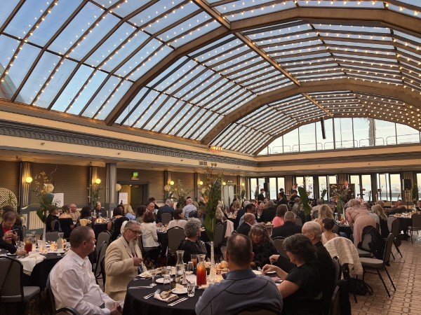 People dining at tables in a large indoor restaurant with a glass dome ceiling and string lights.