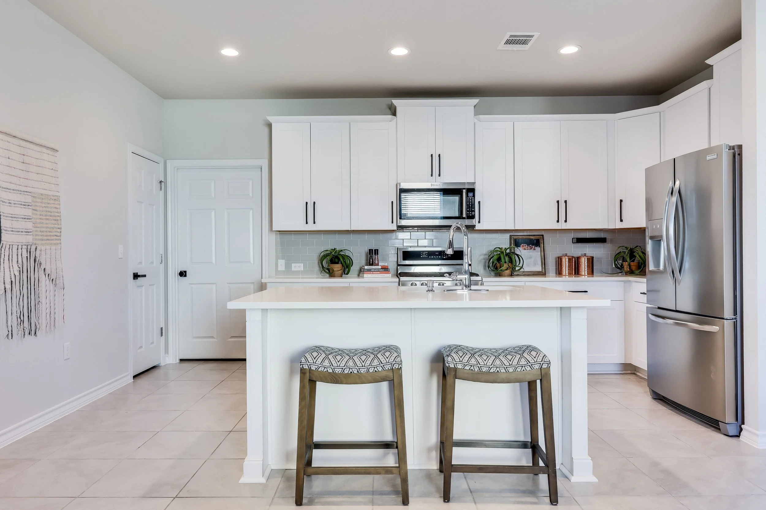 5216 Golden Canary Lane Austin, TX 78723. Modern kitchen with white cabinets, a stainless steel refrigerator, microwave, stove, and a kitchen island with two chairs.