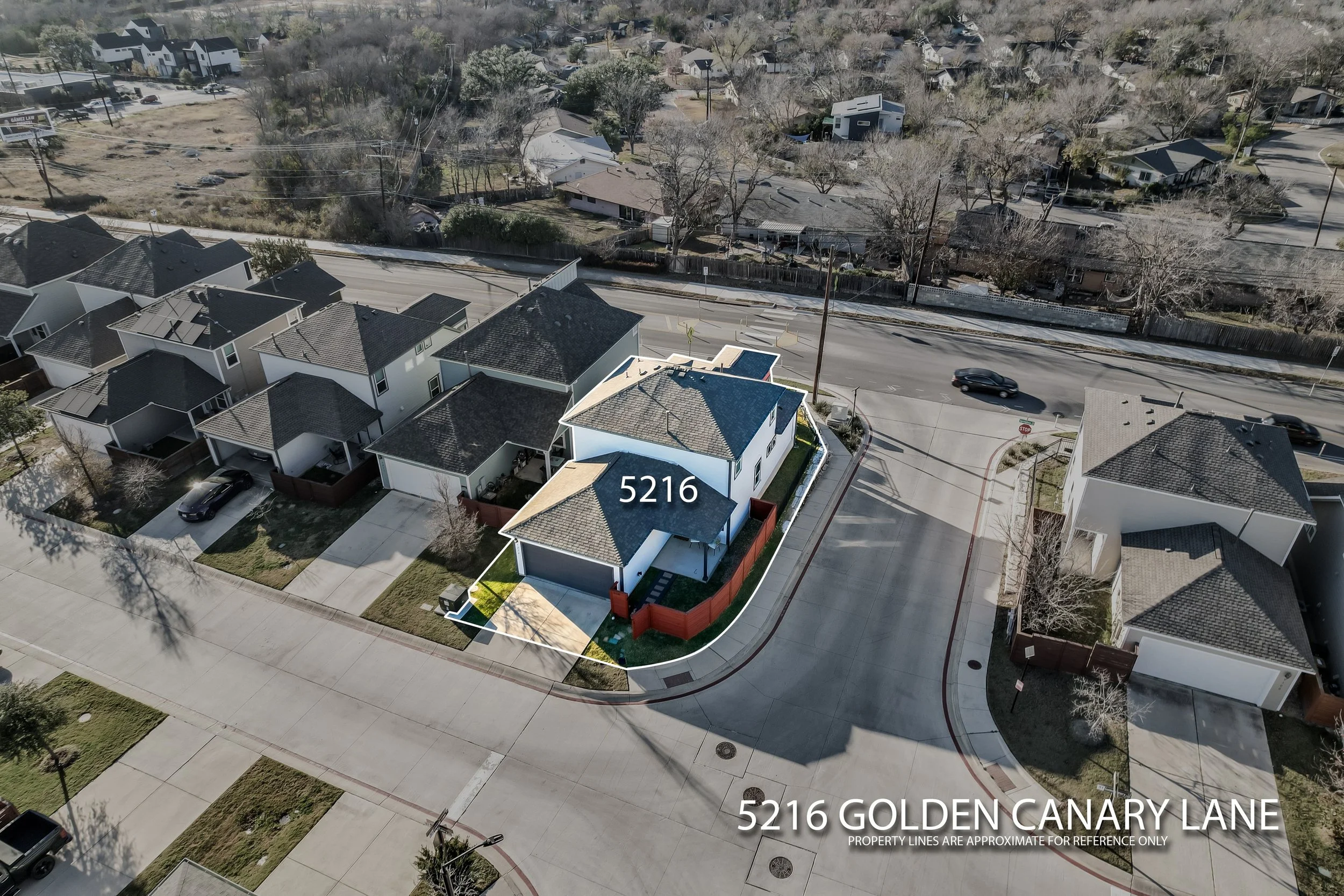 5216 Golden Canary Lane Austin, TX 78723. Aerial view of a residential neighborhood with a focus on a new white house at 5216 Golden Canary Lane, surrounded by other houses and trees, with a curved street and parked cars.