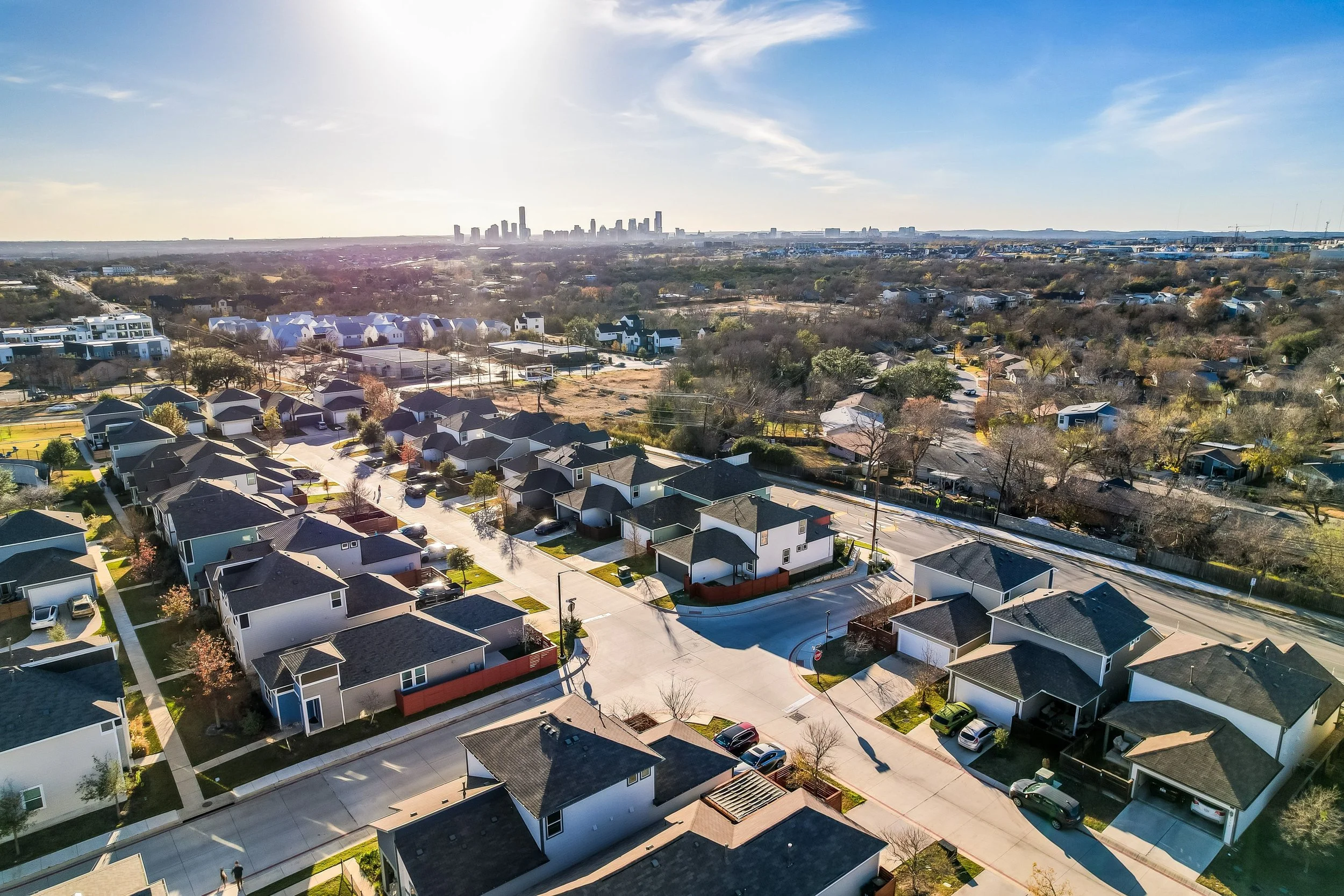 5216 Golden Canary Lane Austin, TX 78723. Aerial view of a suburban neighborhood with houses, streets, trees, and a city skyline in the distance under a clear sky.