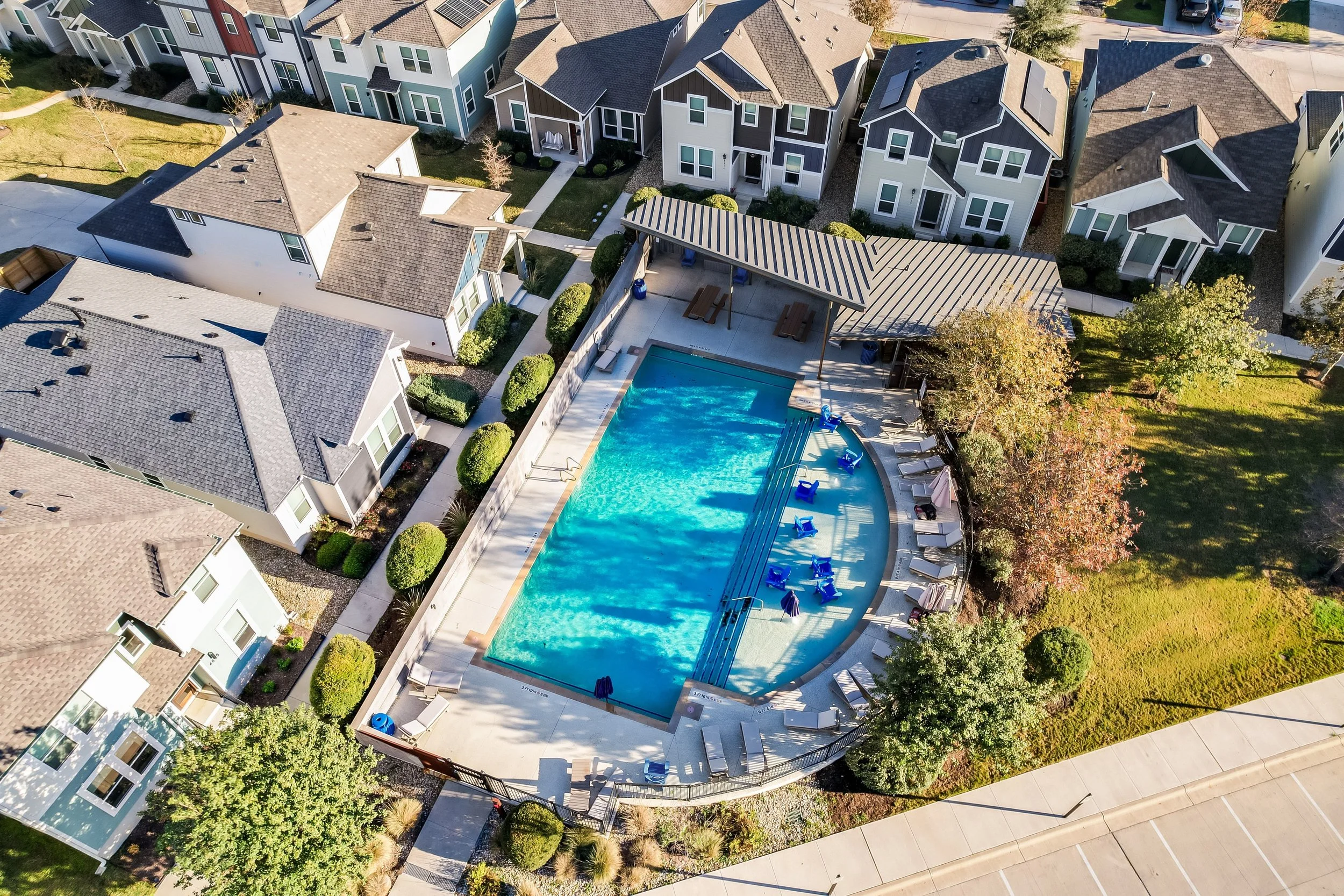 5216 Golden Canary Lane Austin, TX 78723. Aerial view of a residential community with houses surrounding a swimming pool area with lounge chairs and a shaded pavilion.