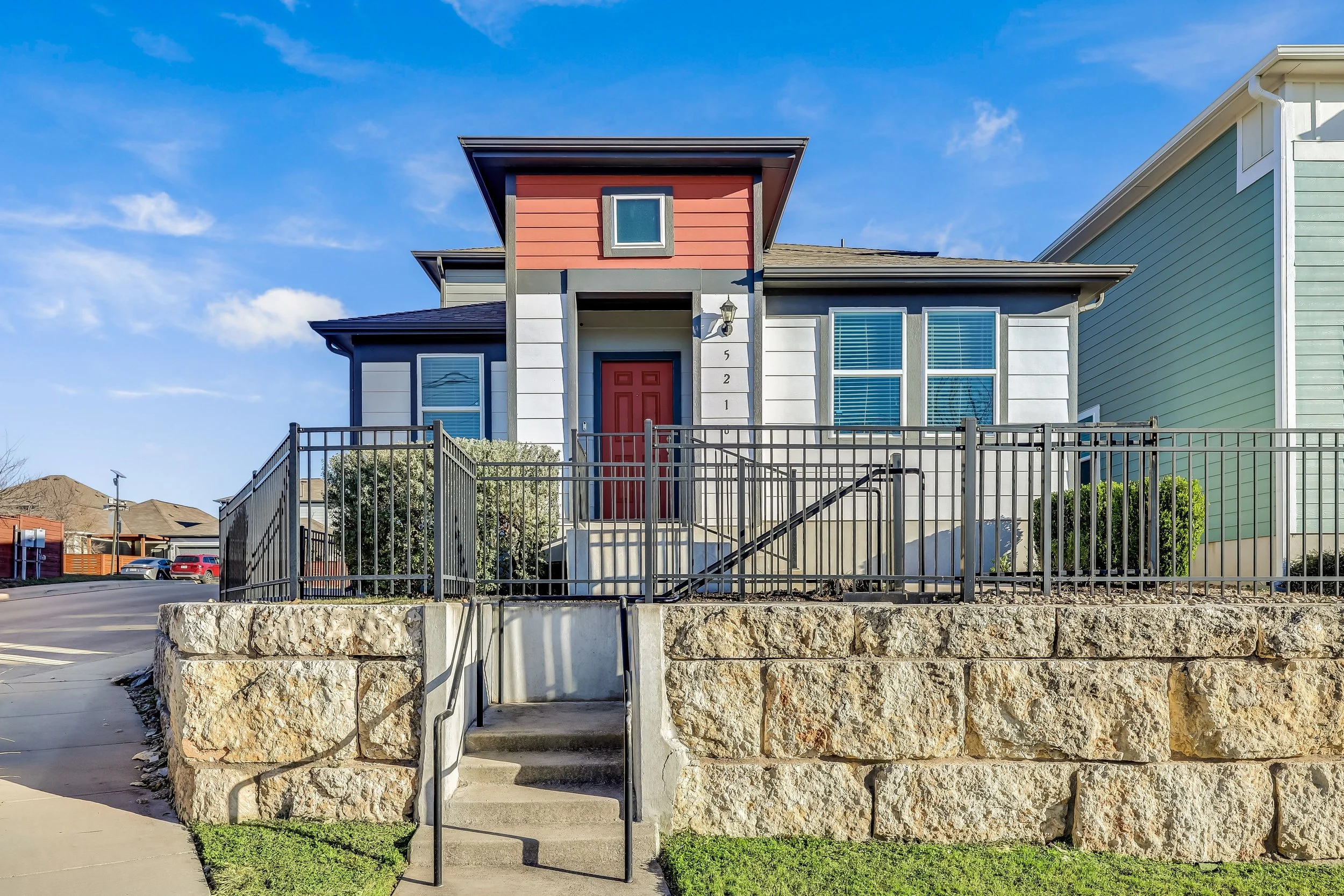 5216 Golden Canary Lane Austin, TX 78723. Front view of a modern house with a raised entrance, gray railing, and stone foundation, under a clear blue sky.
